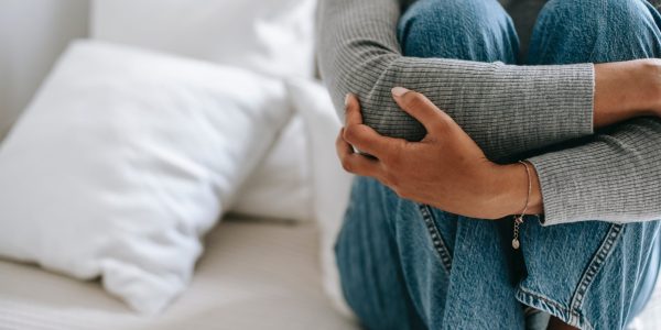 person sitting on bed with knees to chest and arms wrapped around them